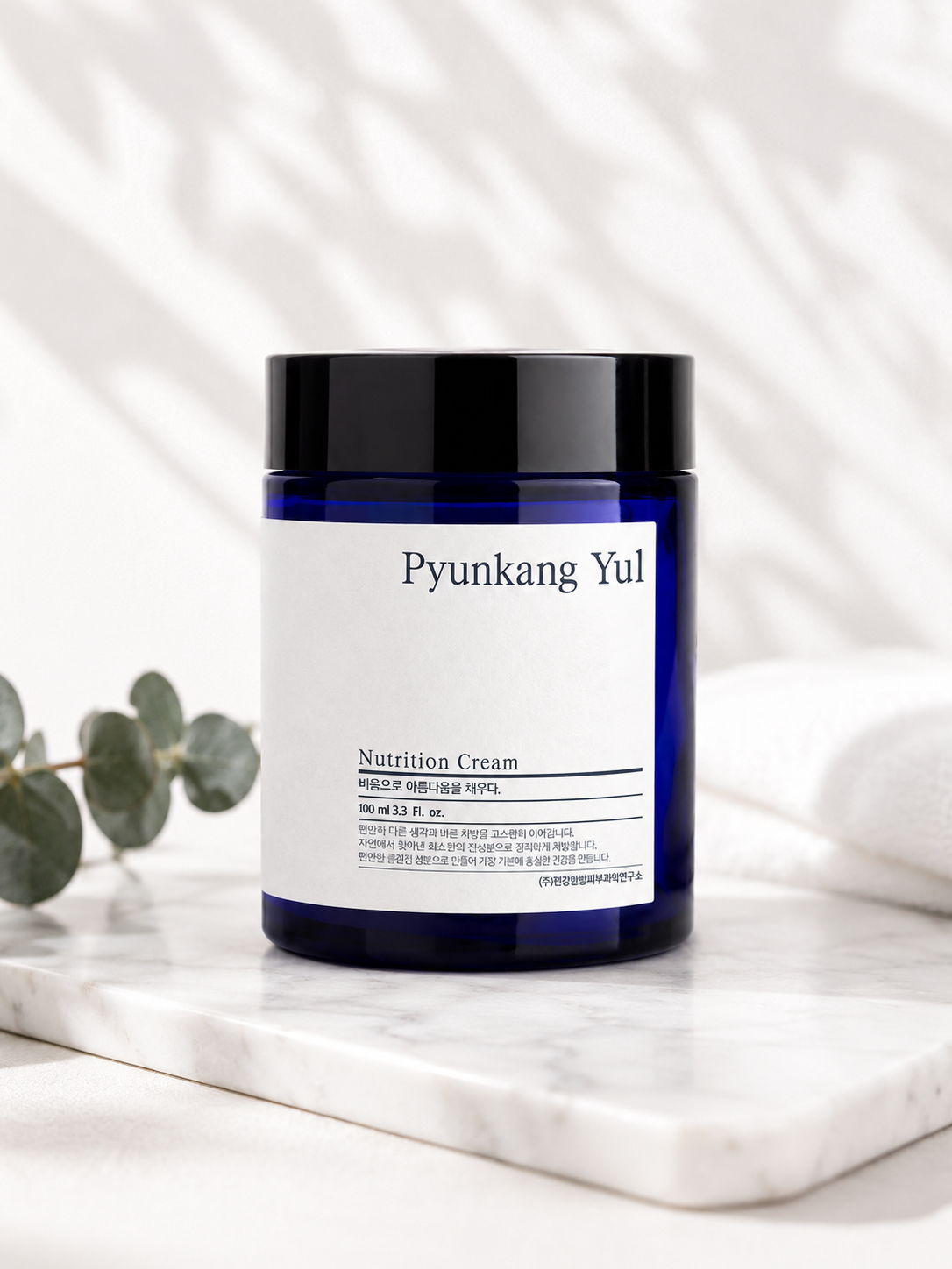 Pyunkang Yul Nutrition Cream 100ml on a marble surface with eucalyptus leaves.