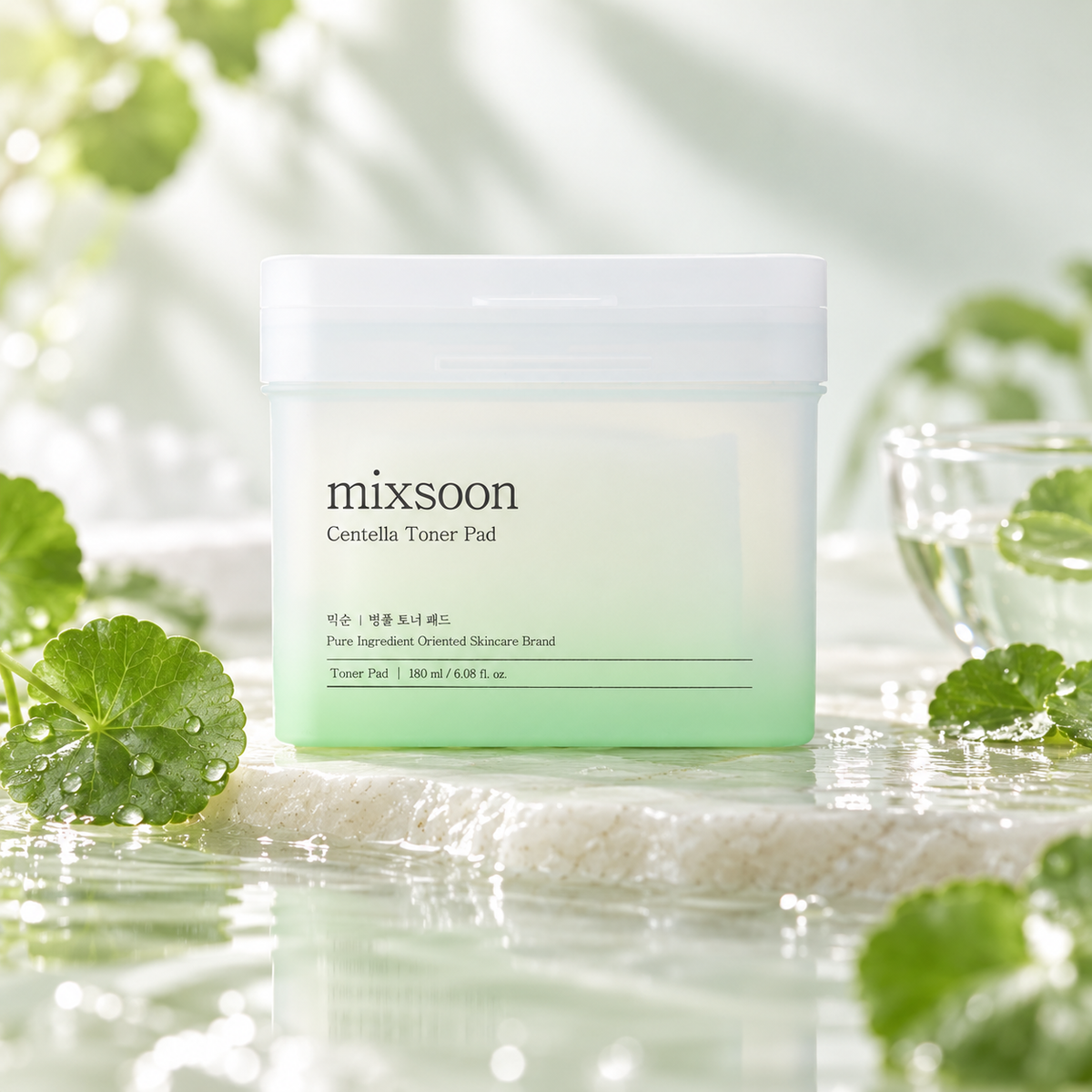 Mixsoon Centella Toner Pad 180ml Korean skincare toner pads in a minimalist white and soft green container, surrounded by fresh Centella Asiatica leaves, delicate water droplets and natural stone. A refreshing K-beauty skincare composition with soft green tones, gentle daylight and a luxurious botanical aesthetic, highlighting soothing hydration and sensitive skin care.