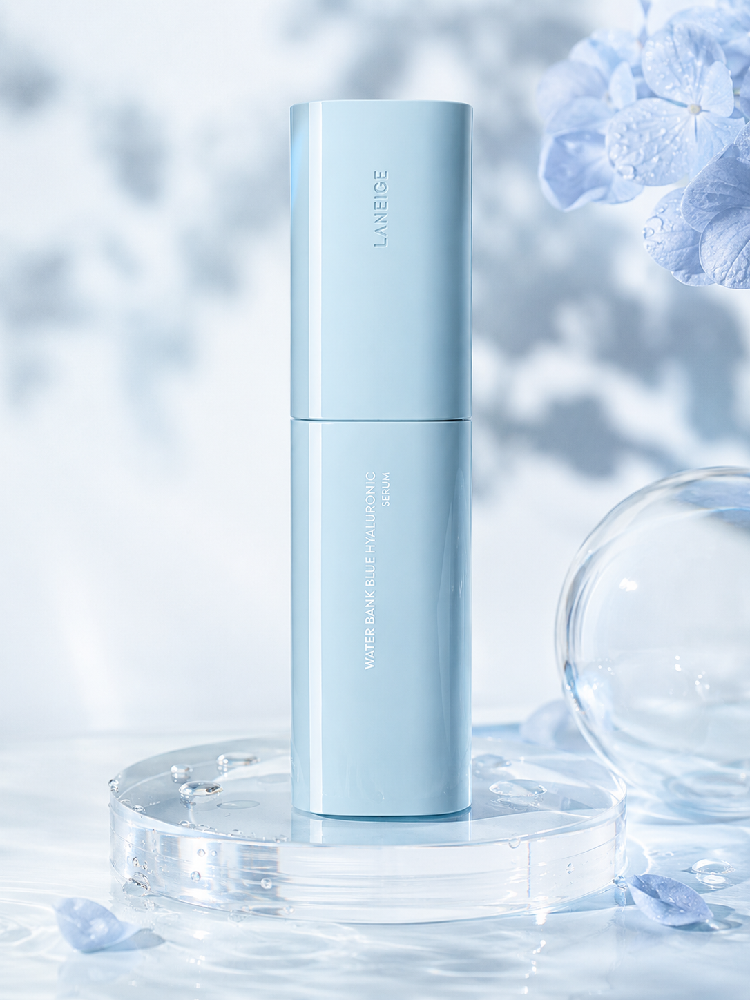 A sleek, light blue serum bottle with a glossy finish stands on a clear glass surface, surrounded by delicate blue flowers and droplets of water, creating a serene atmosphere.